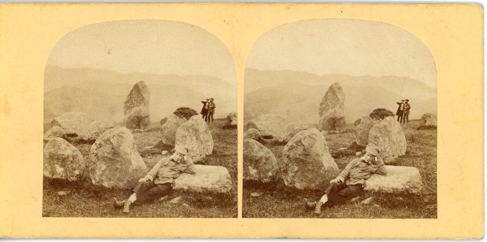 Image of a rectangular stereo photograph showing standing stones viewed by 2 people in the background